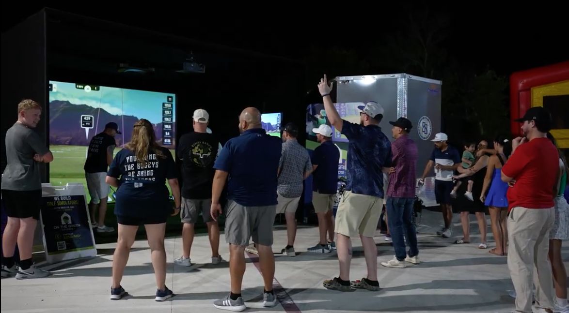 Guests gathered around an On The Green Studios mobile golf simulator at an evening event