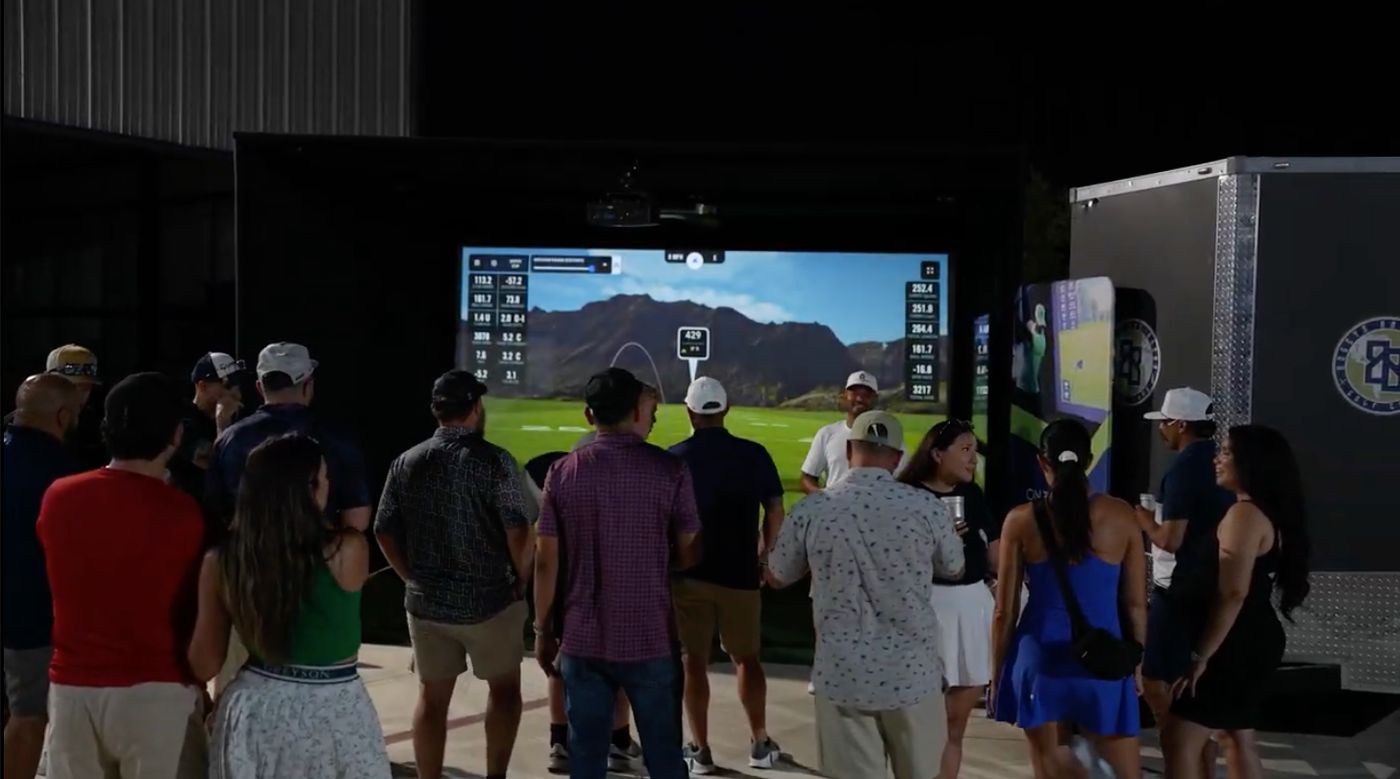 Crowd watching a mobile golf simulator competition at a nighttime event
